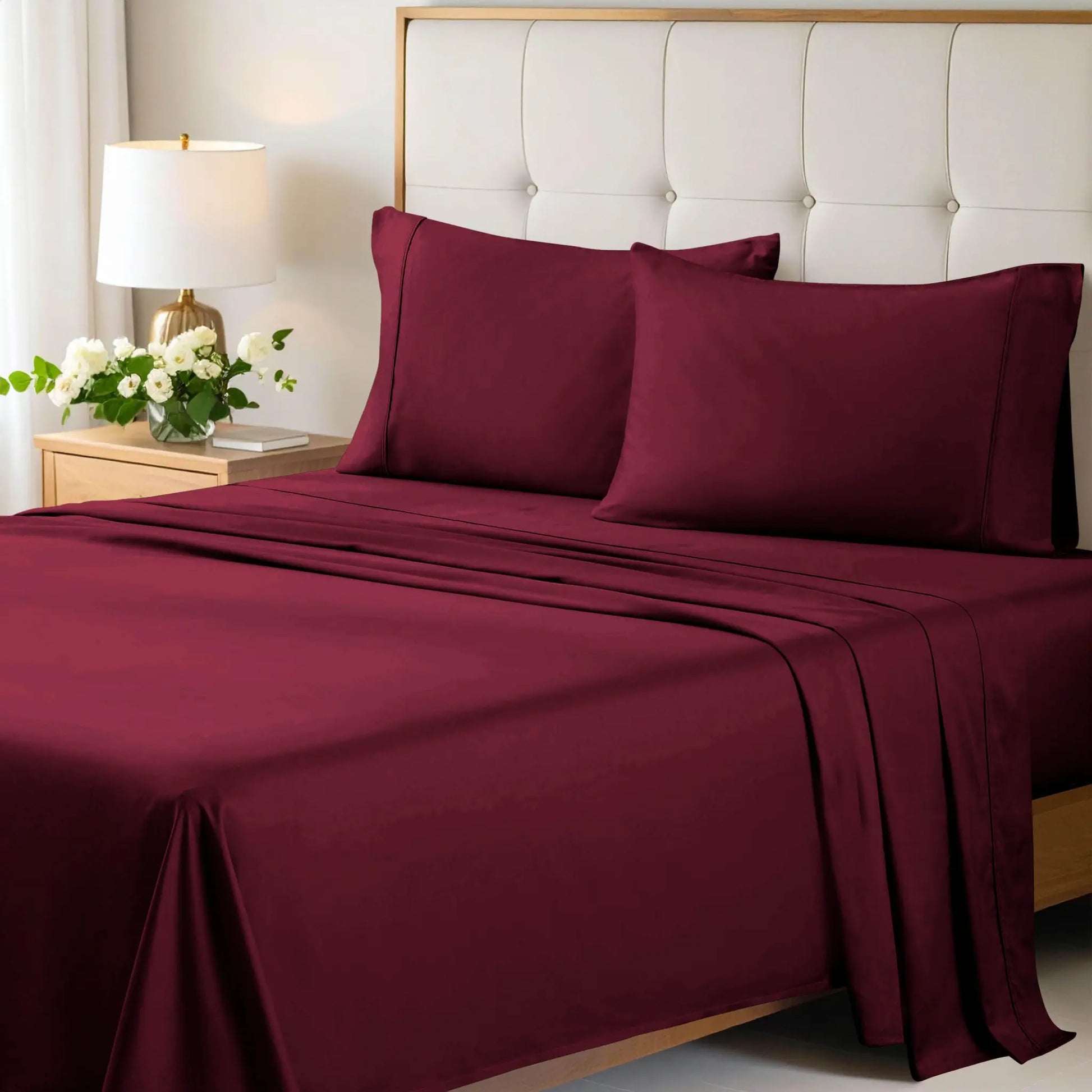 A neatly made bed styled with a burgundy 700 Thread Count Egyptian Cotton Sateen Bed Sheet Set, featuring smooth flat and fitted sheets alongside matching pillows