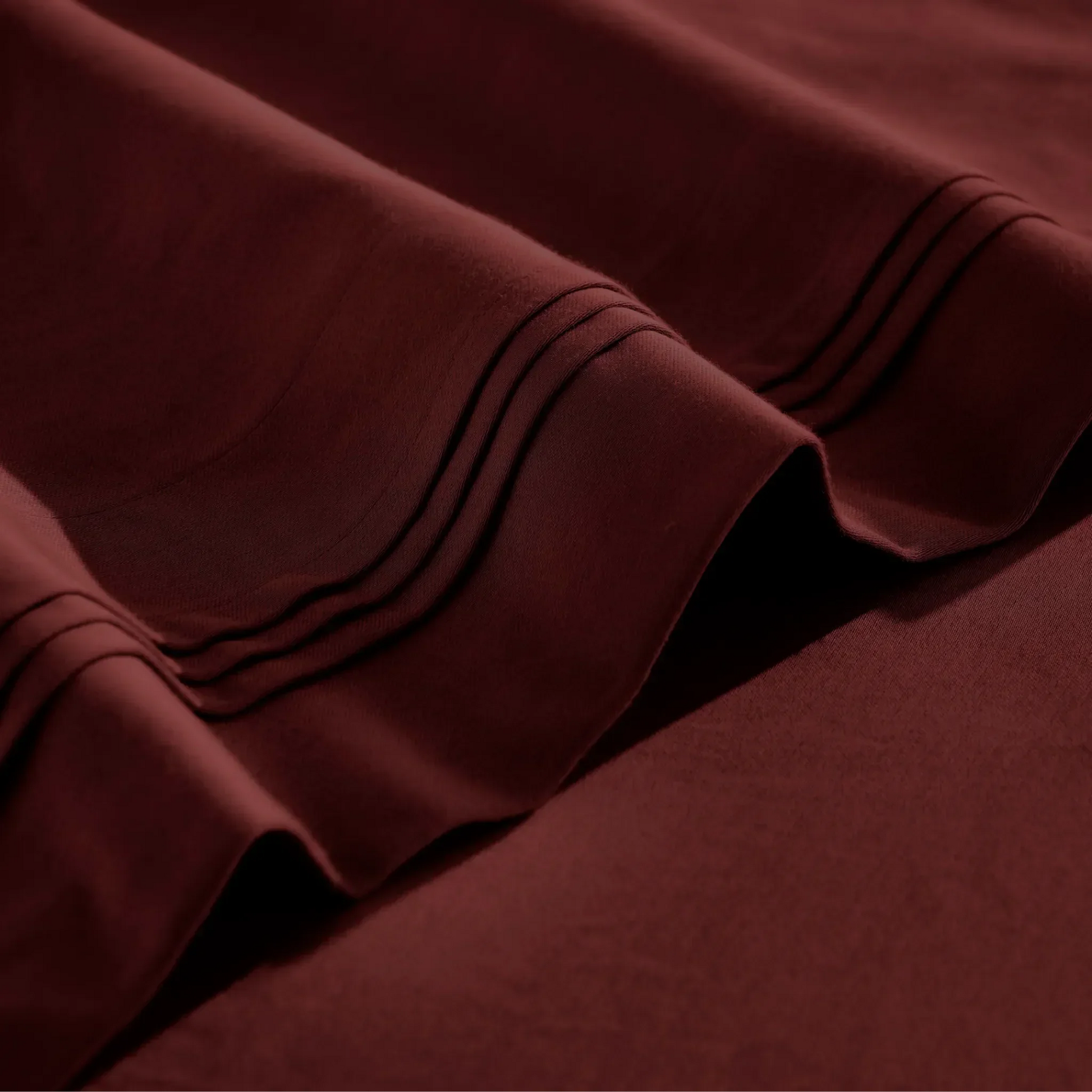 Close-up of Burgundy Egyptian cotton sateen sheet hems with decorative triple-row stitching.