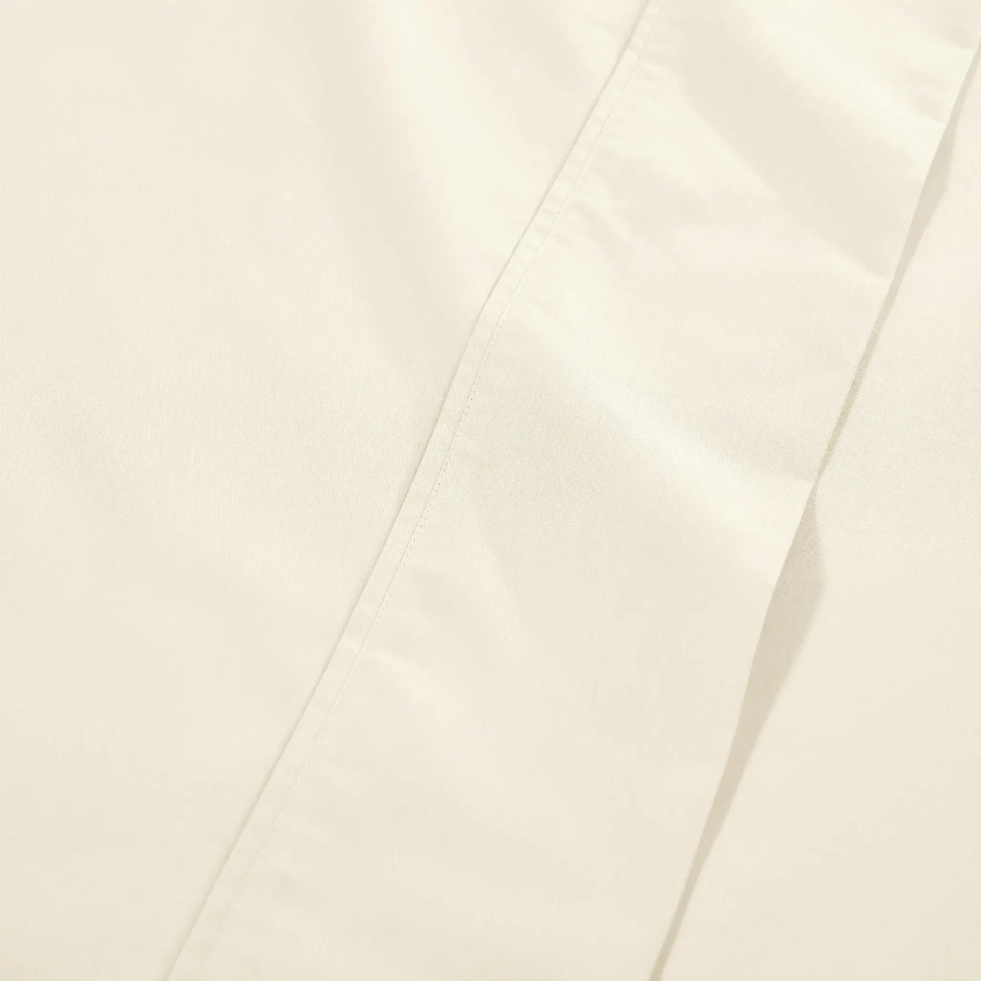 Extreme close-up macro shot of cream cotton blend fabric showing fine weave texture and subtle hem stitching.