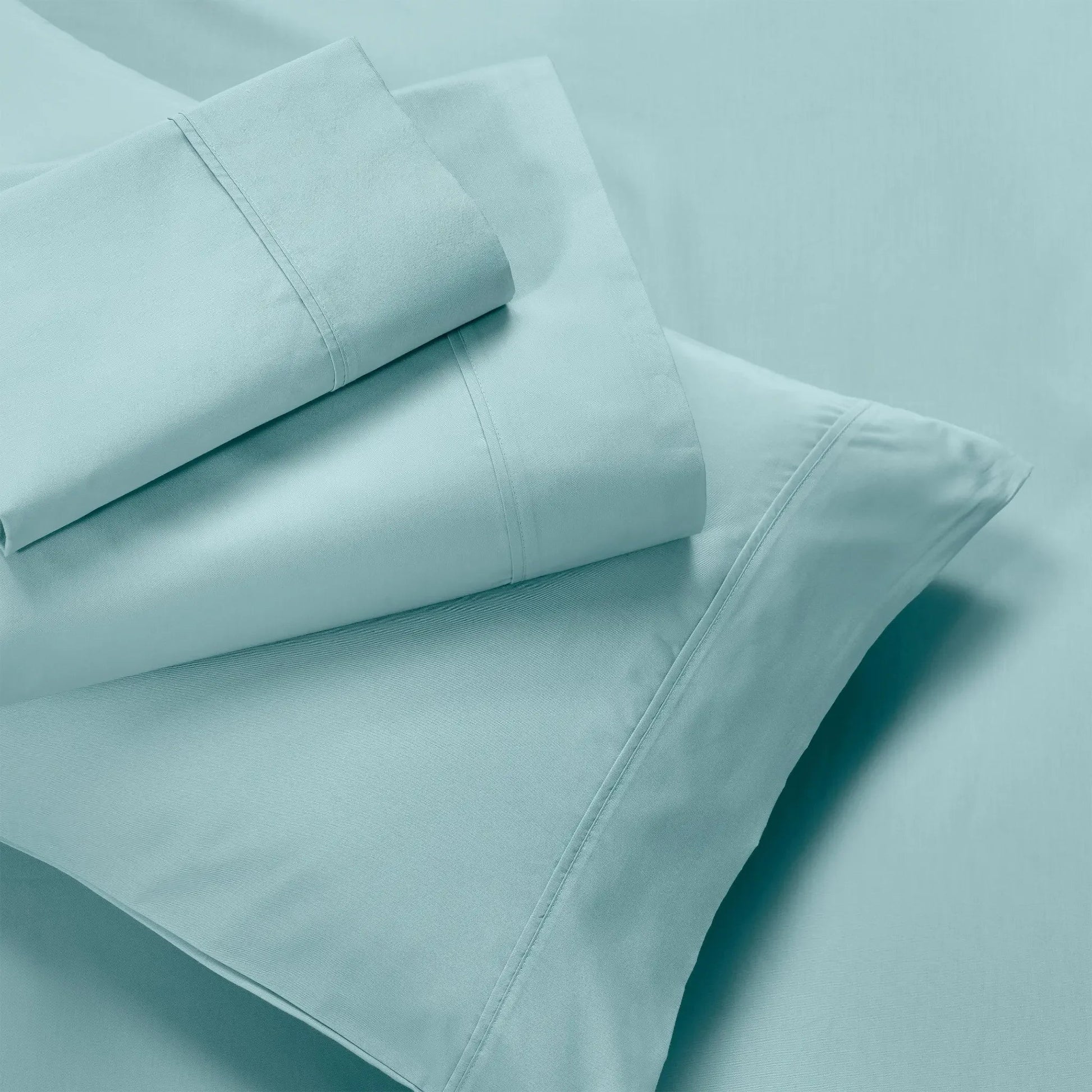 Folded light blue flat sheet, fitted sheet, and pillowcases showing stitched hem borders