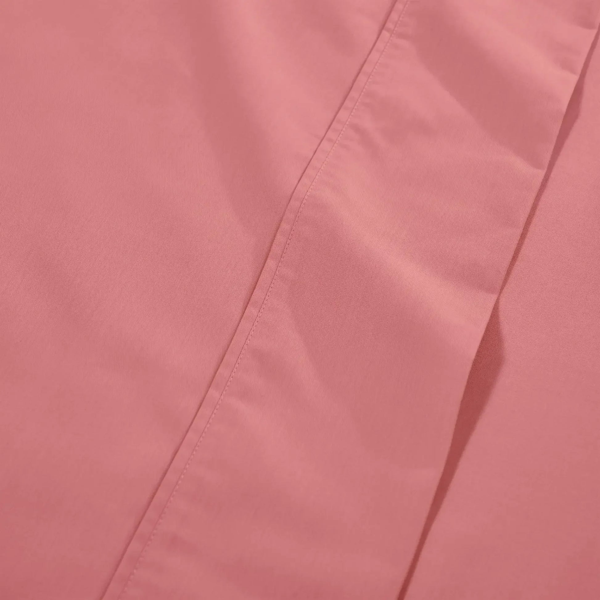 Macro view of solid blush pink bed sheet fabric highlighting the soft matte finish of the material