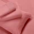 Overhead view of folded blush pink cotton blend bed sheets and matching pillowcase layout
