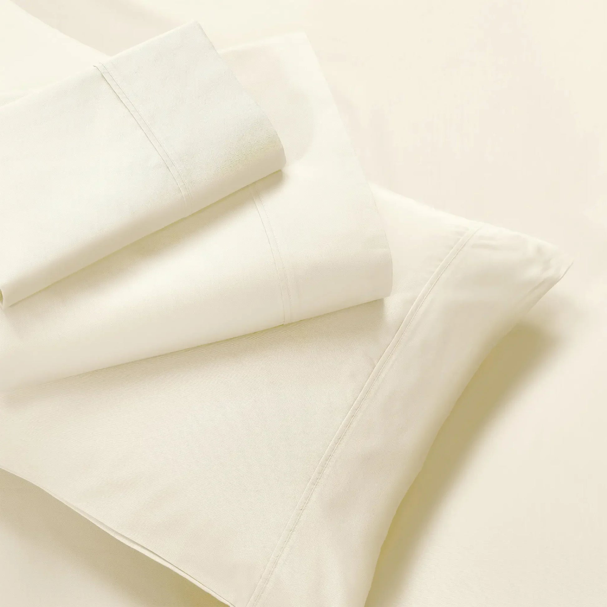 Overhead view of folded cream cotton blend bed sheets and matching cream pillowcase layout.